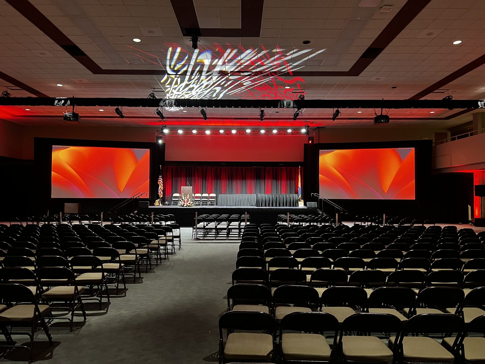 Ceremony & General Session — Dual IMAG screens, red theatrical uplighting and stage set for a formal ceremony.